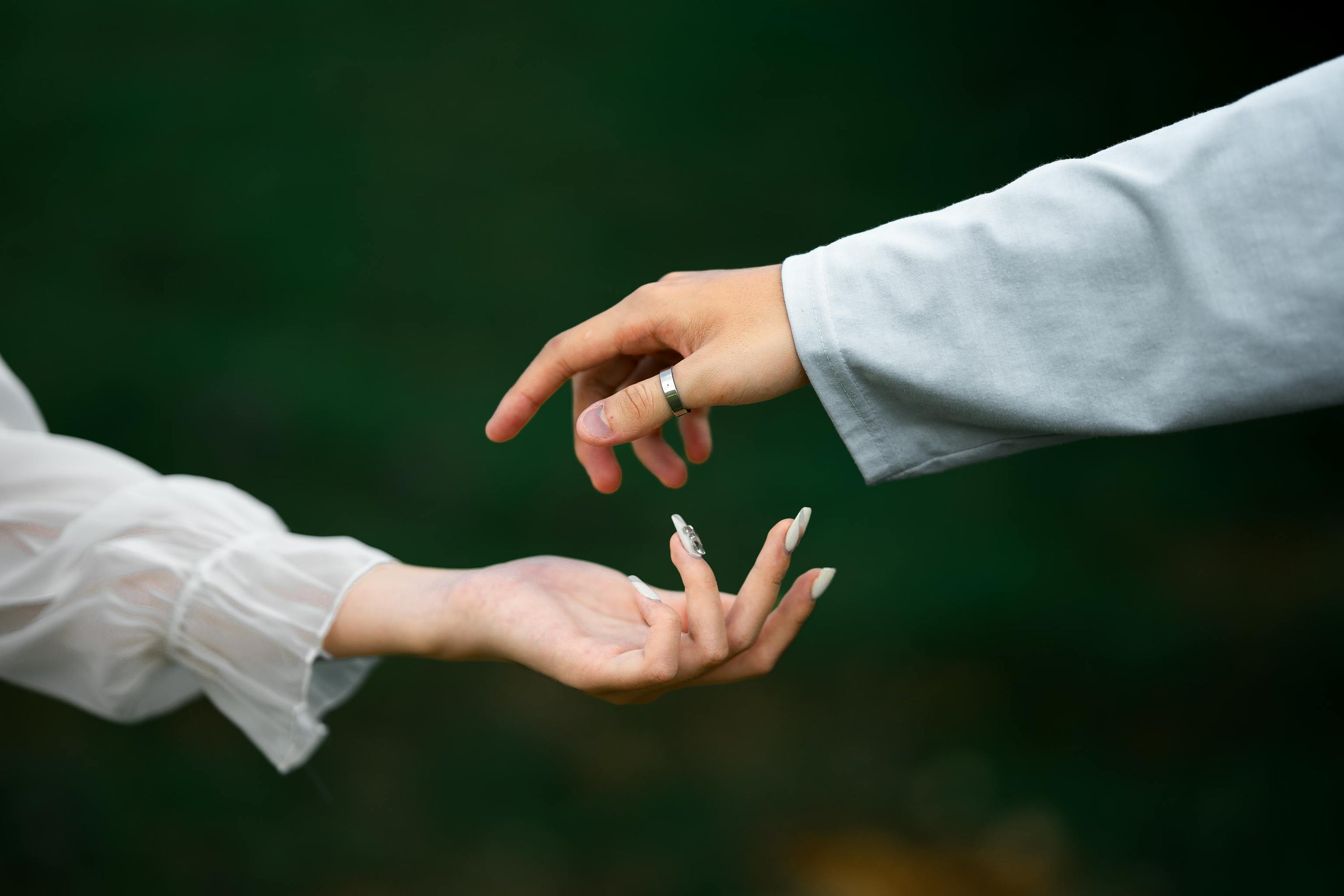 Two people reaching toward each other, one hand wearing a wedding ring, with a blurred green background