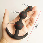 Black silicone butt plug held in a hand with measurements indicated