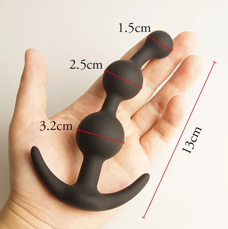 Black silicone butt plug held in a hand with measurements indicated