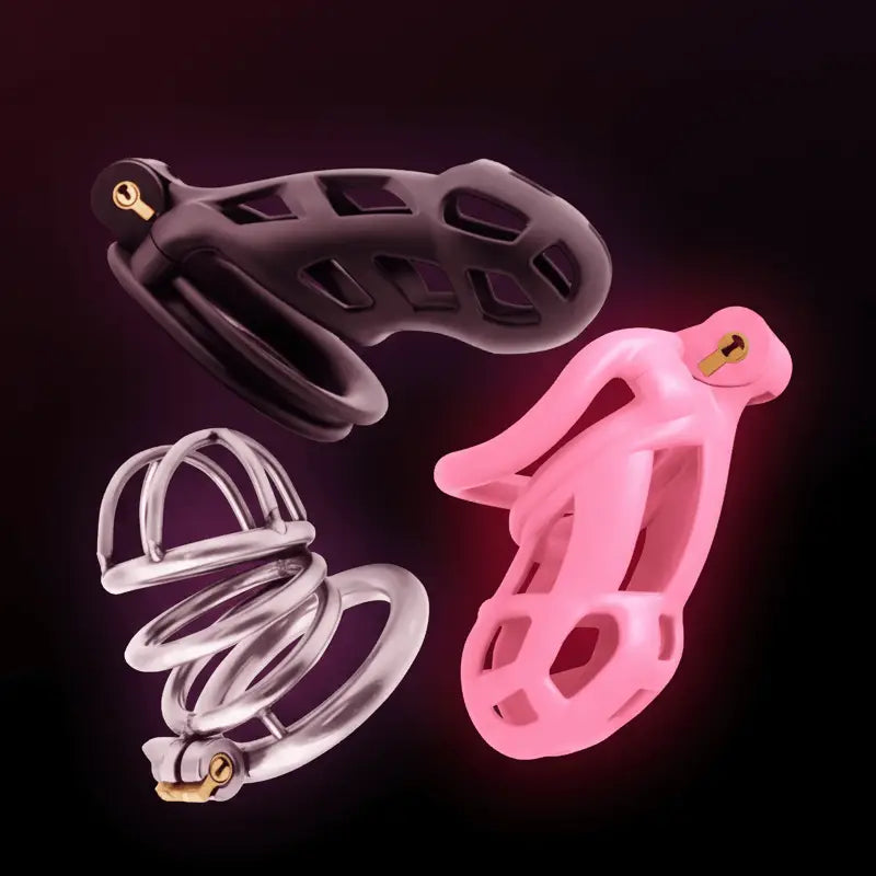 Three silicone and metal chastity cage in black, pink, and clear on a dark background